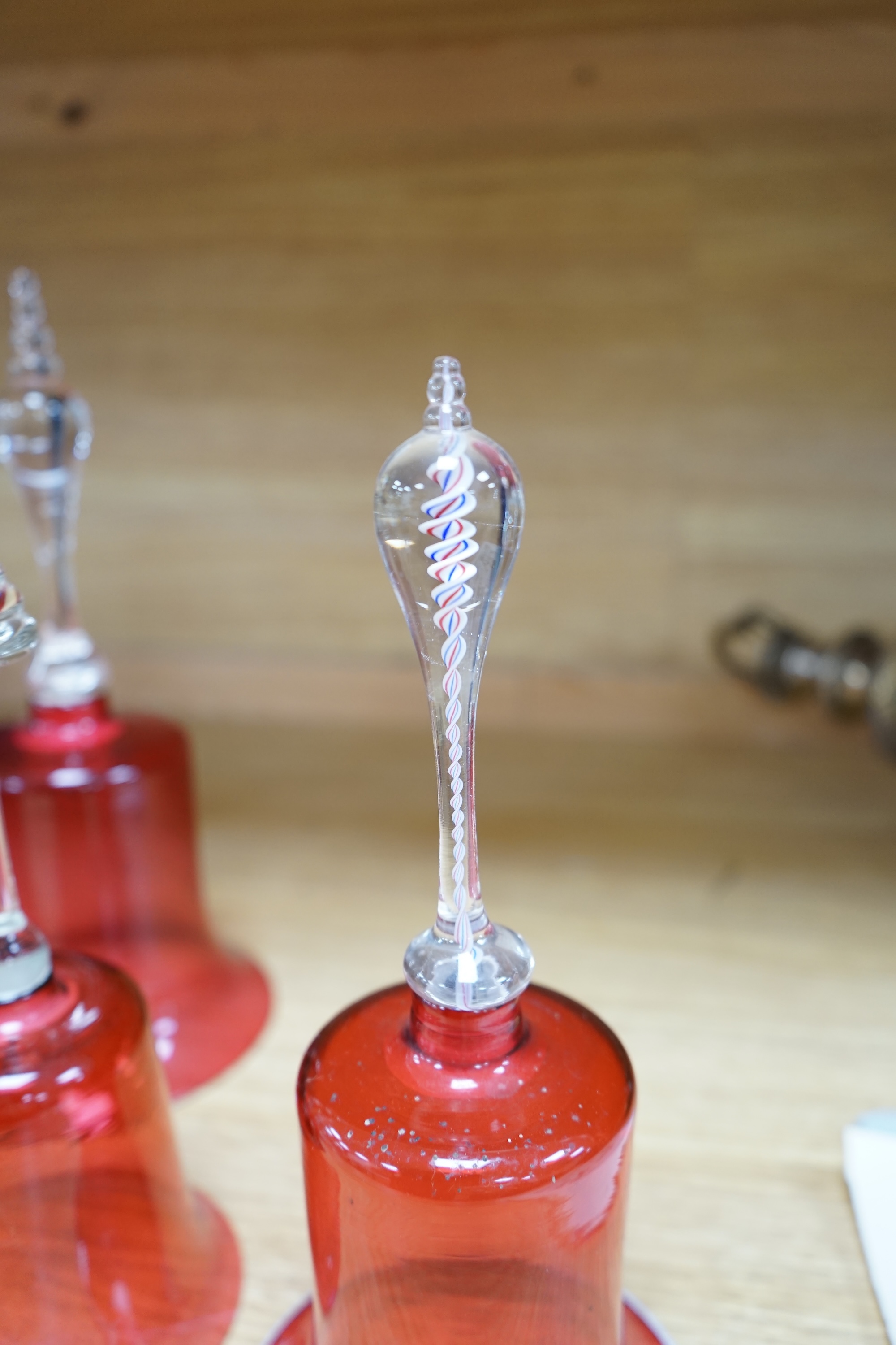 Seven 19th century cranberry glass hand bells, various sizes, largest 30.5cm high. Condition - fair